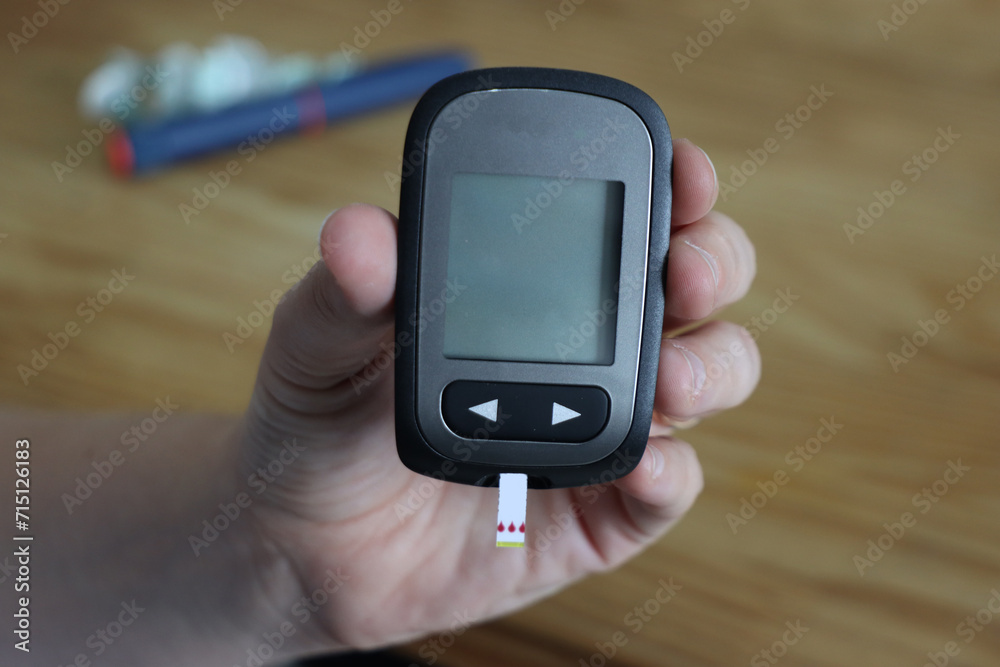 Glucometer been showed in the front with insulin pen and needles in the background. Glucometer screen beeing showed with copy space