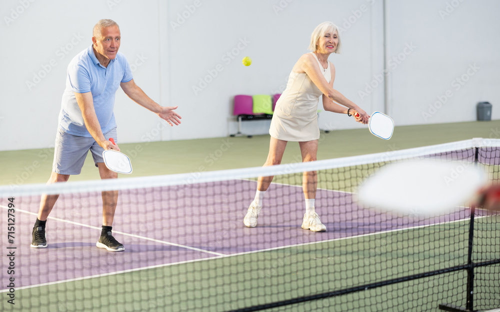 Two pickleball players prepare to return a ball on a pickleball court indoor