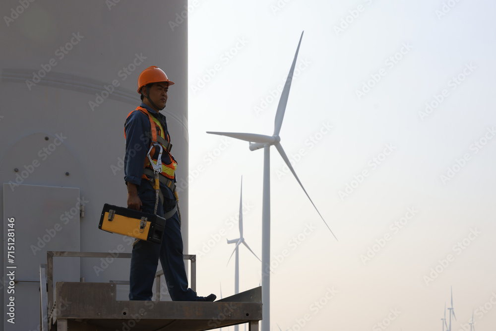 Specialist wind turbine technician working at the base of the turbine. Wind turbine service technician wearing safety uniform and safety harness working at windmill farm