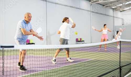 Two athletic men of different ages are playing a game of pickleball on a court inside a sports facility