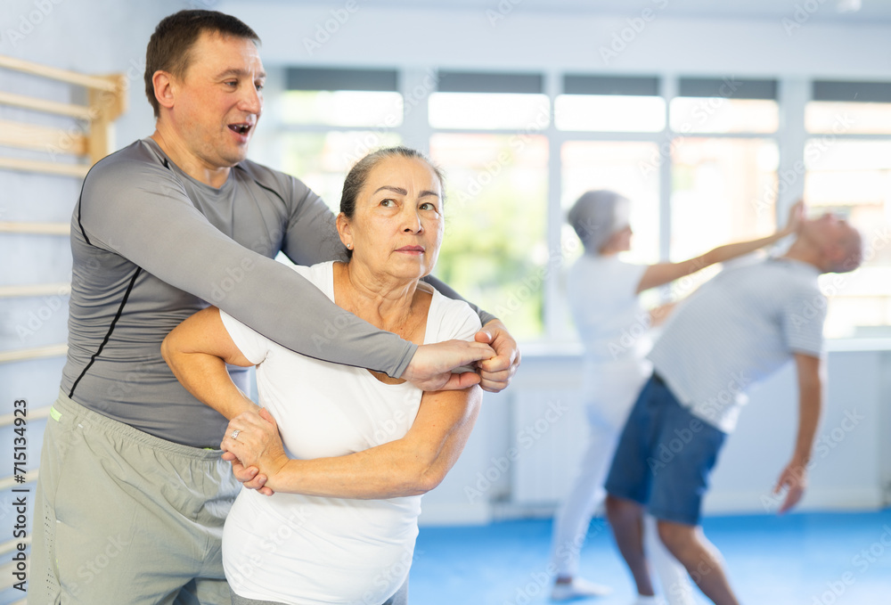 Fototapeta premium Aggressive old woman practicing self-defense techniques in pairs during workout session