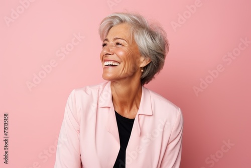 Portrait of happy senior woman looking away and laughing against pink background