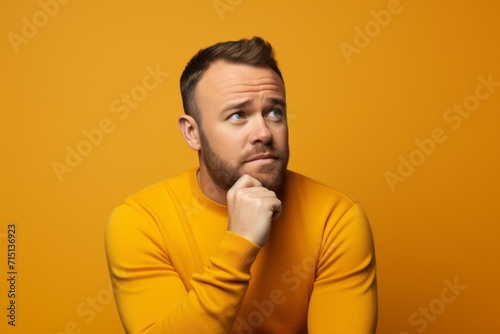 Portrait of pensive man in yellow sweater on yellow background.