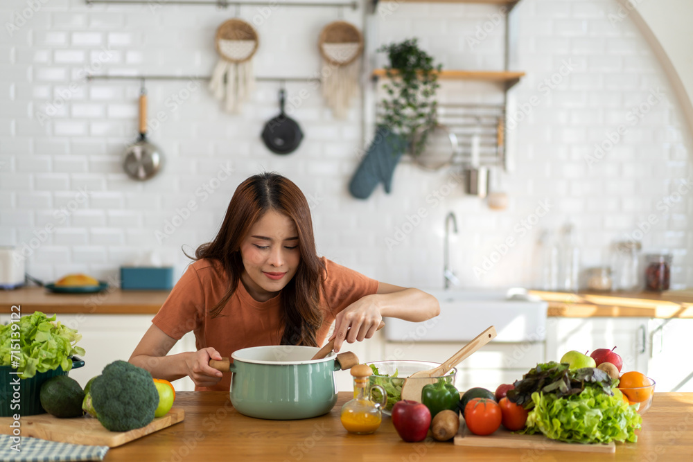 Young woman standing near stove and cooking, housewife, meal, chef, food.Happy woman looking and smelling tasting fresh delicious from soup in a pot with steam at white interior kitchen.
