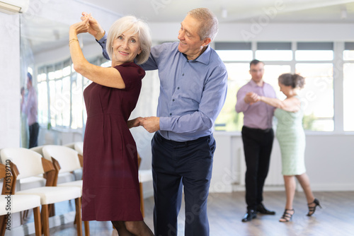 Happy mature woman enjoying impassioned merengue with male partner in latin dance class. Social dancing concept photo