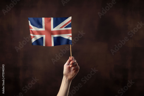 Female hand holding a United Kingdom flag in front of a brown background. celebration. patriotic concept.