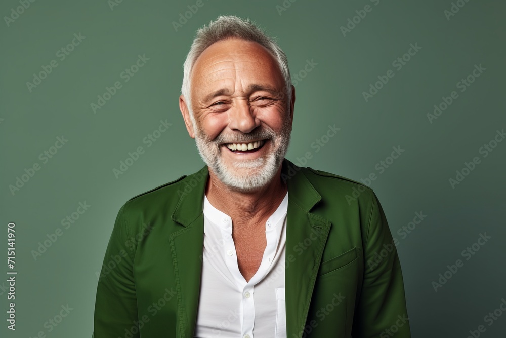 Handsome senior man smiling and looking at camera while standing against green background