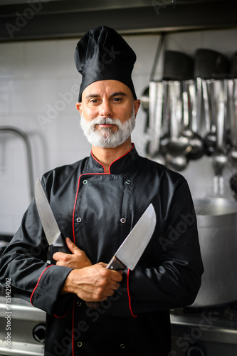 Confident chef posing with knives in kitchen