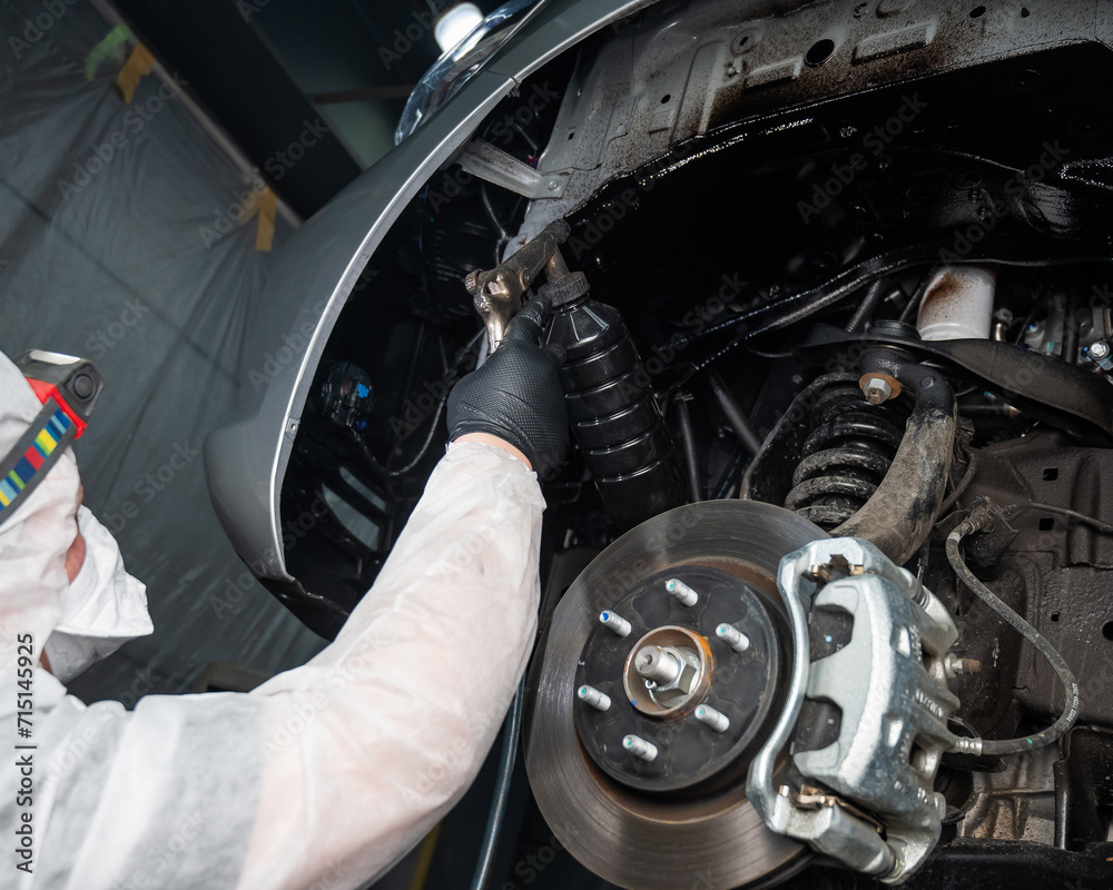 An auto mechanic applies anti-corrosion mastic to the underbody of a car. An auto mechanic applies anti-corrosion mastic to the underbody of a car.
