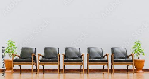 Fototapeta Naklejka Na Ścianę i Meble -  Row of five wooden chairs with black cushions near pots on white wall and cafe floor stage