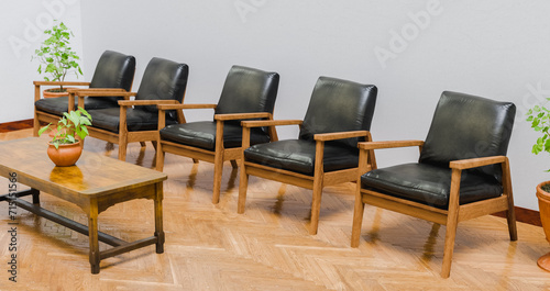 Waiting room with five wooden chairs with black cushions and a table with pots, spaces and interiors