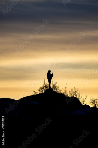 person oor adventurer on top of a hill photographing the sunset with a smartphone or iPhone