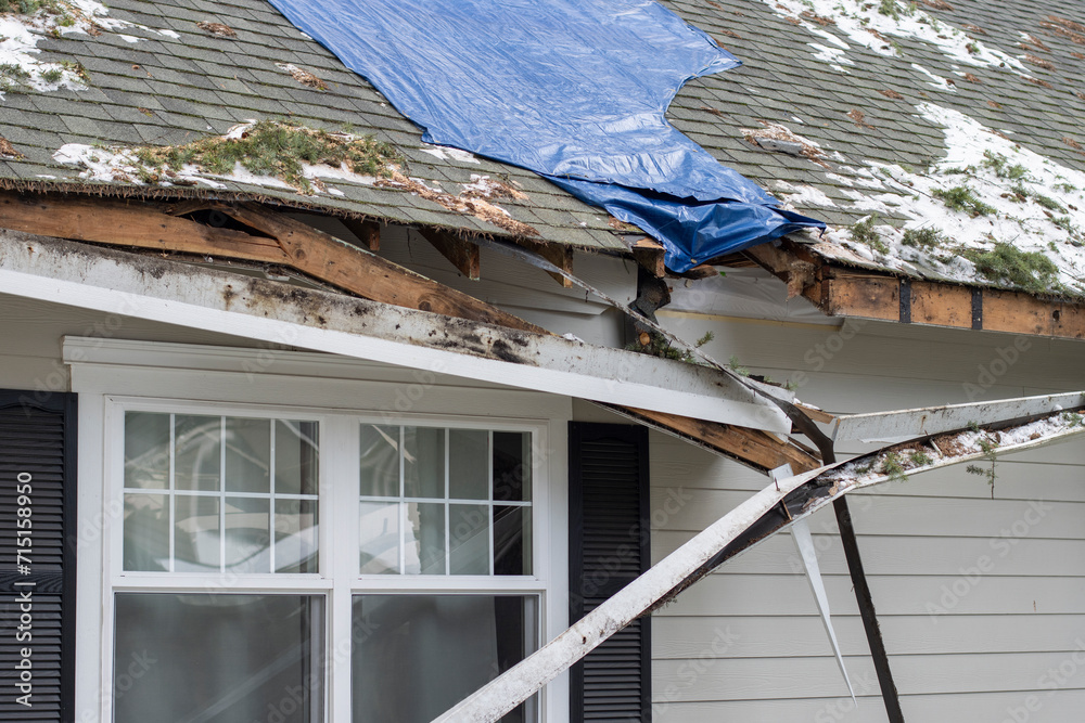 Residential house crushed by fallen trees and tree limbs during severe winter storm with strong winds. Tarp is placed on the damaged rooftop area as a temporary measure before proper roof repairs. - obrazy, fototapety, plakaty 
