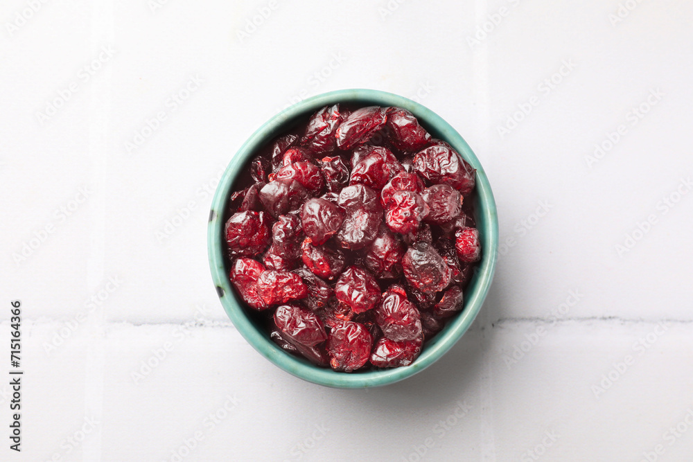 Tasty dried cranberries in bowl on white tiled table, top view Tasty dried cranberries in bowl on white tiled table, top view