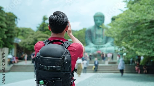 Back view of unrecognizable Hispanic male tourist standing in casual clothes with backpack standing in front of Kotoku-in in Buddhist temple in Kamakura Tokyo in daylight, Japan photo