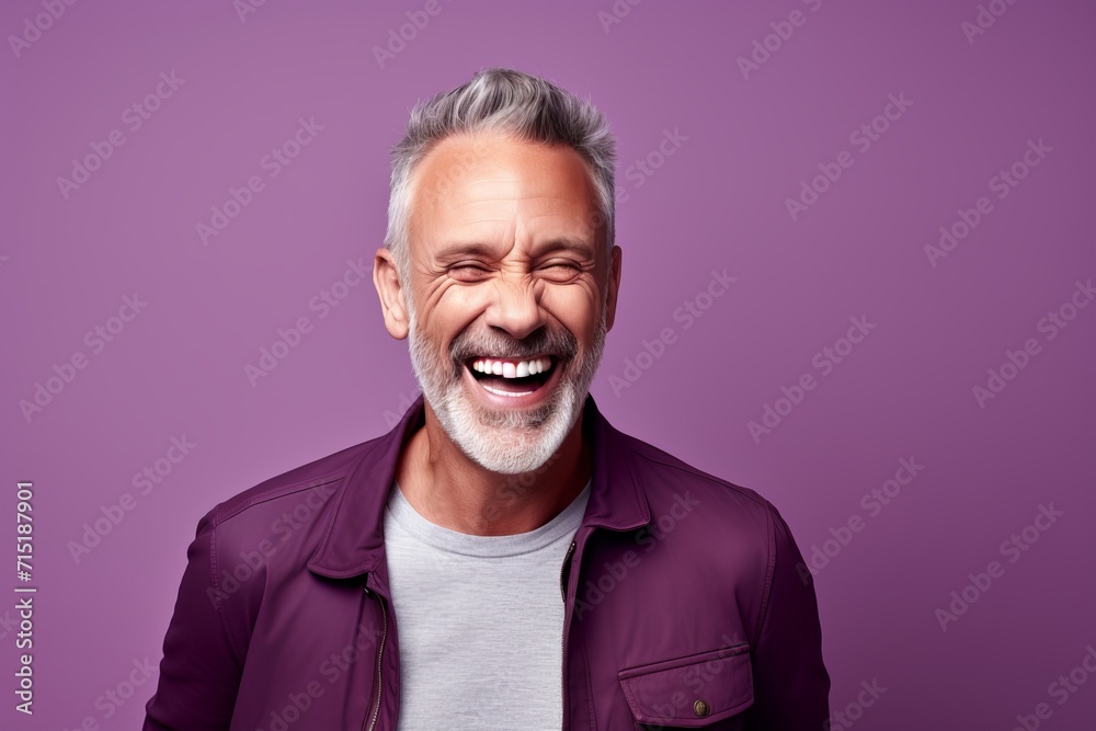 Portrait of happy mature man with grey hair and beard looking at camera and laughing while standing against purple background Portrait of happy mature man with grey hair and beard looking at camera and laughing while standing against purple background
