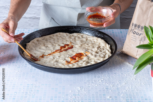 Putting tomato sauce on a homemade pizza.