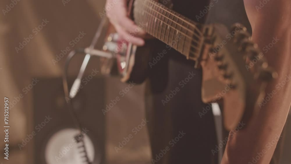 Tilt-up slowmo of young Caucasian hipster man with electric guitar plugging multiple audio cables into modular synthesizer while playing in studio