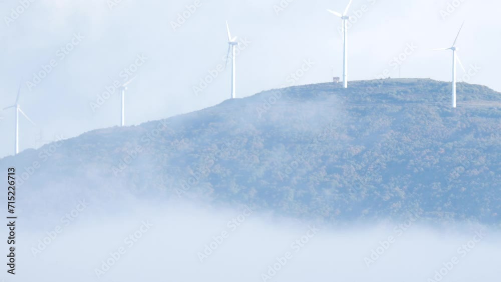 Wind turbines farm on hill in foggy landscape. Windmill covered with white clouds in the morning. Blue ecological power energy generation. Wind turbines farm on hill in foggy landscape. Windmill covered with white clouds in the morning. Blue ecological power energy generation.