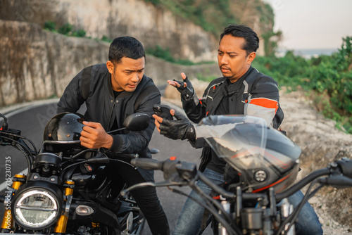 asian male riders sitting on motorbike and conversating seriously while holding phone photo