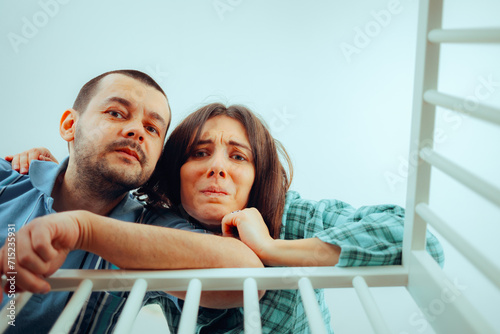 Worried Parents Looking into the Crib Having Mixed Feelings. New mom and dad overthinking and feeling confused about parenting 
 photo