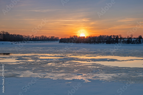 Landscape with winter sunset by the frozen river.