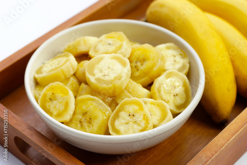 Banana slices in white bowl on wooden tray.