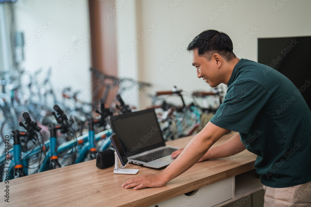 male shop assistant stands while working with laptop computer in bicycle shop male shop assistant stands while working with laptop computer in bicycle shop