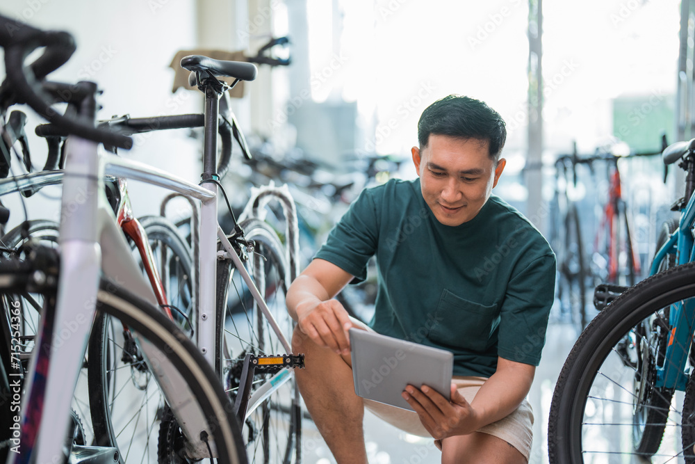 young male owner uses a tablet while squatting in a bike shop young male owner uses a tablet while squatting in a bike shop