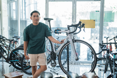 Asian male employee stands holding a wrench next to a new bike while working at a bike shop