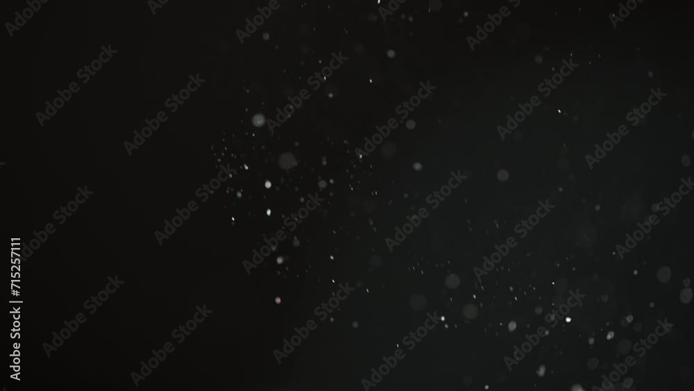 Abstract macro particles floating upwards on a black background in slow motion