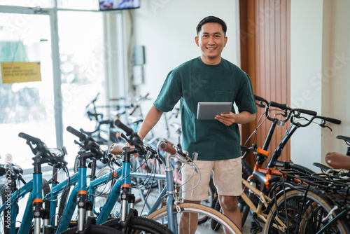 entrepreneurial man stands smiling at the camera holding a digital tablet in a bicycle shop