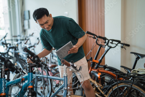 young man looks at the new model of a bicycle while using a tablet at a bicycle shop