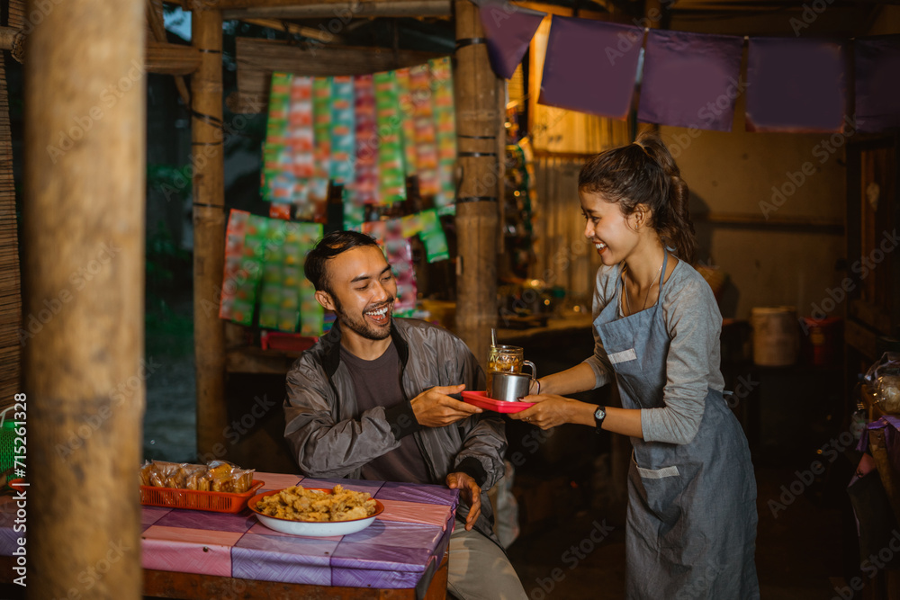 male customers are happy when a female stallholder gives them a drink at a traditional stall