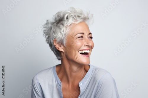 Portrait of a happy senior woman laughing and looking up against grey background