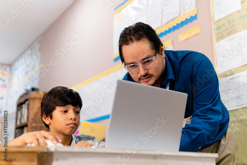 Diverse male teacher and schoolboy using laptop in elementary school class