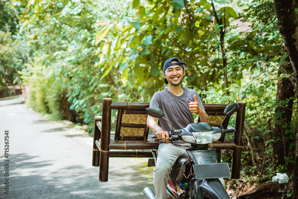 salesman smiles with thumbs up carrying a bamboo chair on motorcycle on the road