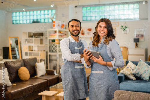 smiling female and male shop assistants in aprons look at the camera standing in a furniture store