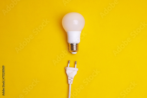 Light bulb and electrical plug on yellow background. Concept of saving energy by using LED lamp photo