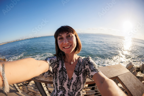 A young and cheerful girl in a dress takes a selfie on the beach. © zhukovvvlad