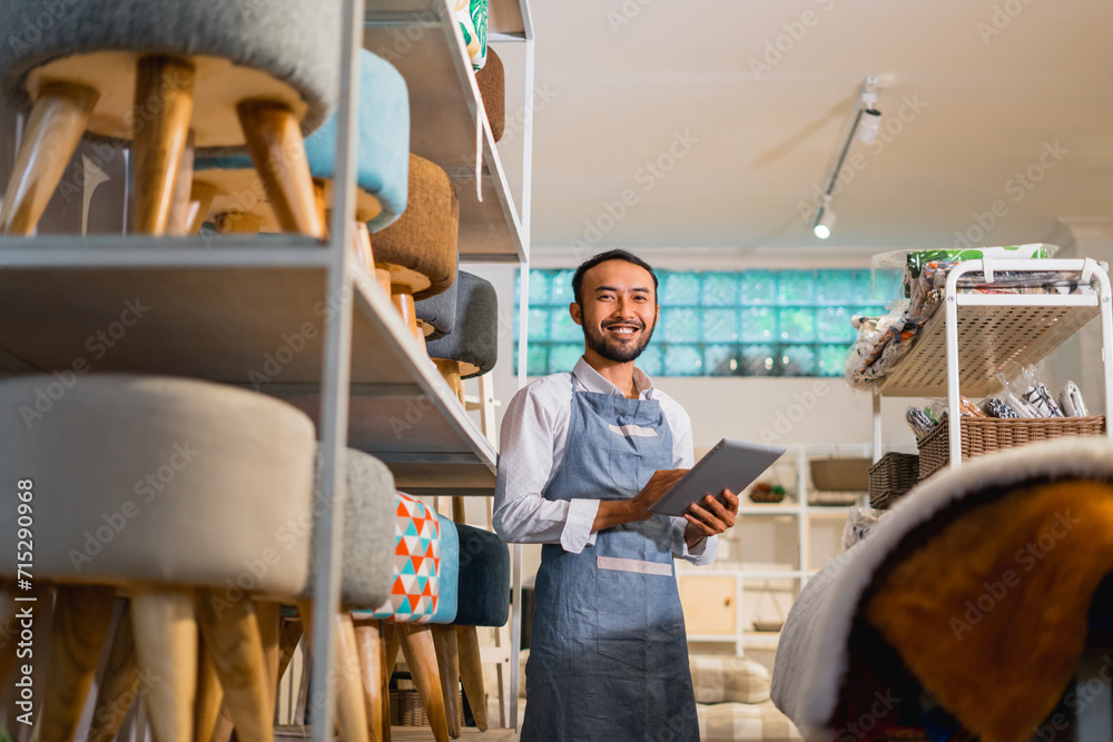shopkeeper man in apron smiles while holding a tablet at a furniture store