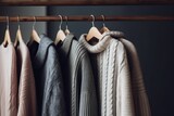 Assorted sweaters and jackets on wooden hangers against a dark background.