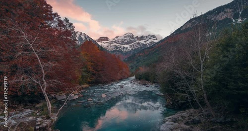 Sunset timelapse in Bujaruelo Valley with snowy high peaks colorful fall autumn trees and pristine blue river pyrenees mountains photo