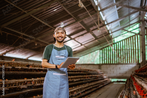 smiling young Asian entrepreneur using a pad standing on chicken farm
