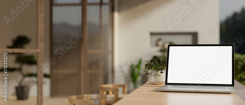 A white-screen laptop computer mockup on a wooden dining table in a cosy, Scandinavian room. photo