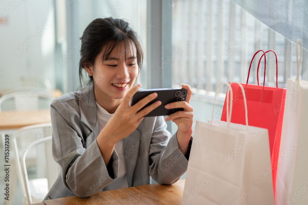 Happy Asian woman is enjoying playing a mobile game while relaxing in a cafe in a shopping mall.