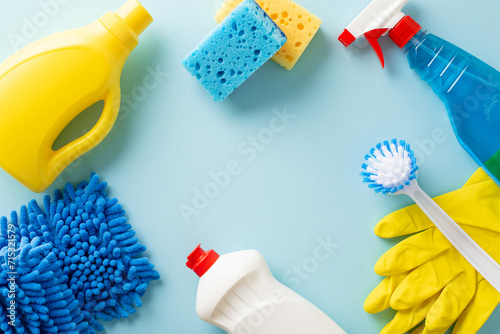 Home cleaning essentials showcased on pastel blue backdrop. Top view image featuring scrub brush, sponges, gloves, detergents, sprayer— perfect depiction of cleanliness. Empty space for your message