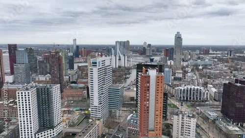 The drone is flying over tall buildings with the Erasmus brigde in the background an a cloudy day in Rotterdam The Netherlands Aerial Footage 4K photo