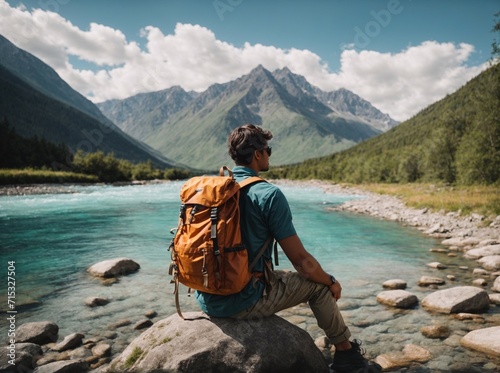 A man with a tourist backpack sitting on a stone against a river in the mountains