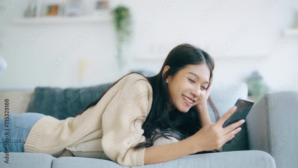 Happy young asian woman relaxing at home. Female smile lying on sofa and holding mobile smartphone. Girl using video call to friend Happy young asian woman relaxing at home. Female smile lying on sofa and holding mobile smartphone. Girl using video call to friend